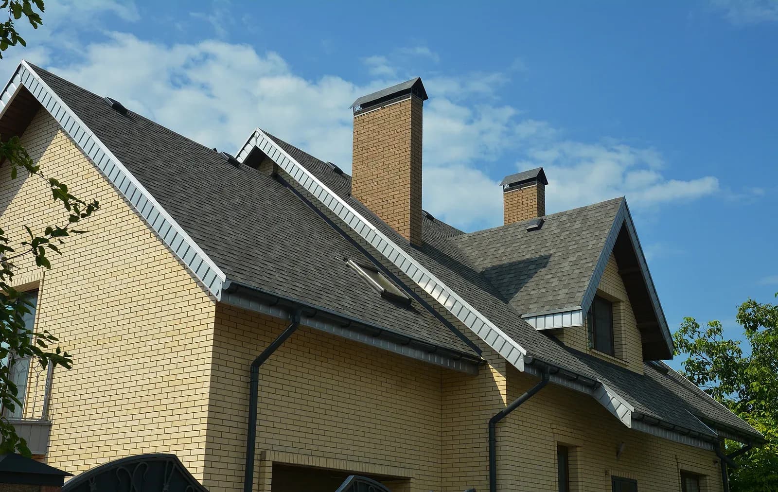 A photo of the roof of a brown brick house with two chimneys and black gutters.