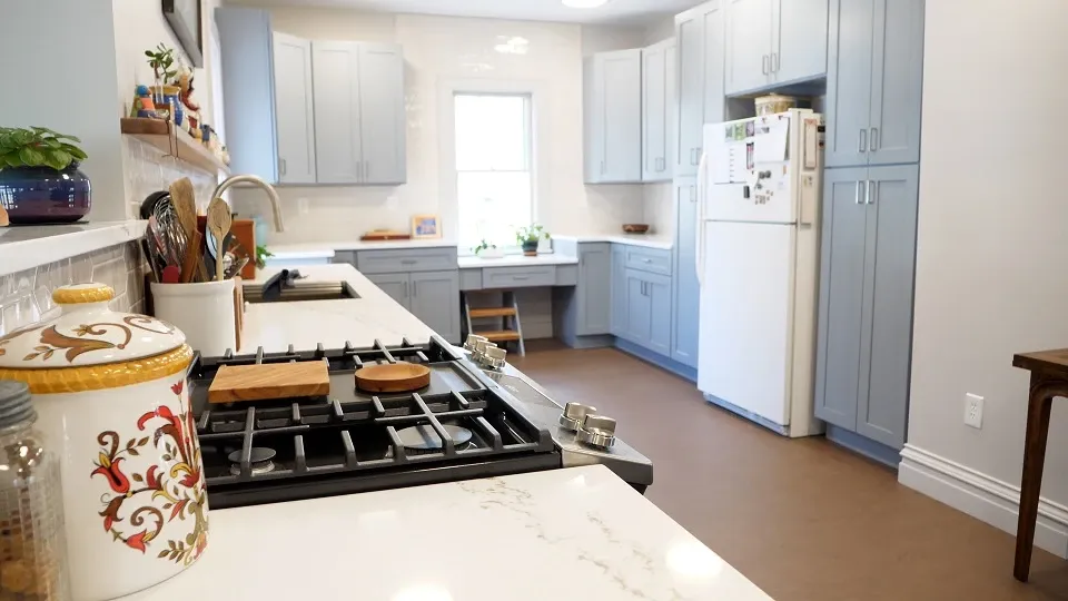 A view of the kitchen from the counter. The updated range is visible in the foreground, and the fridge and gray cabinets are in the background.
