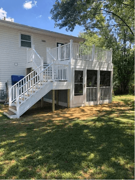 White elevated house with wraparound deck and white stairs, surrounded by green lawn and trees on a sunny day