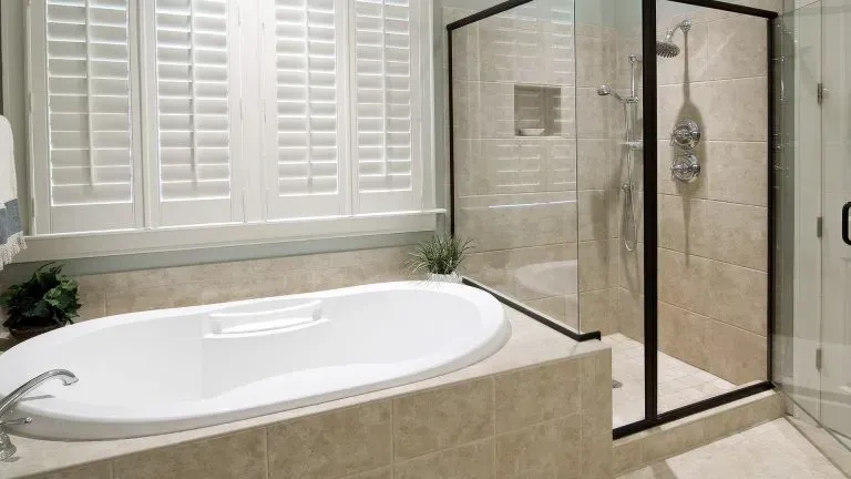 A photo of a large bathtub with a glass shower to the right surrounded by tan stone tile.