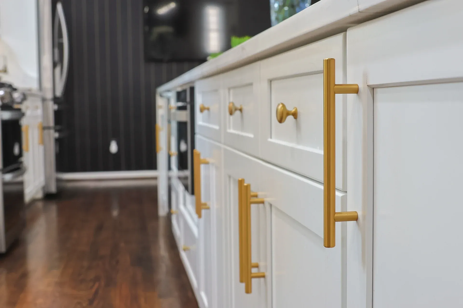 A close up view looking down a line of white cabinets with gold-colored fixtures.