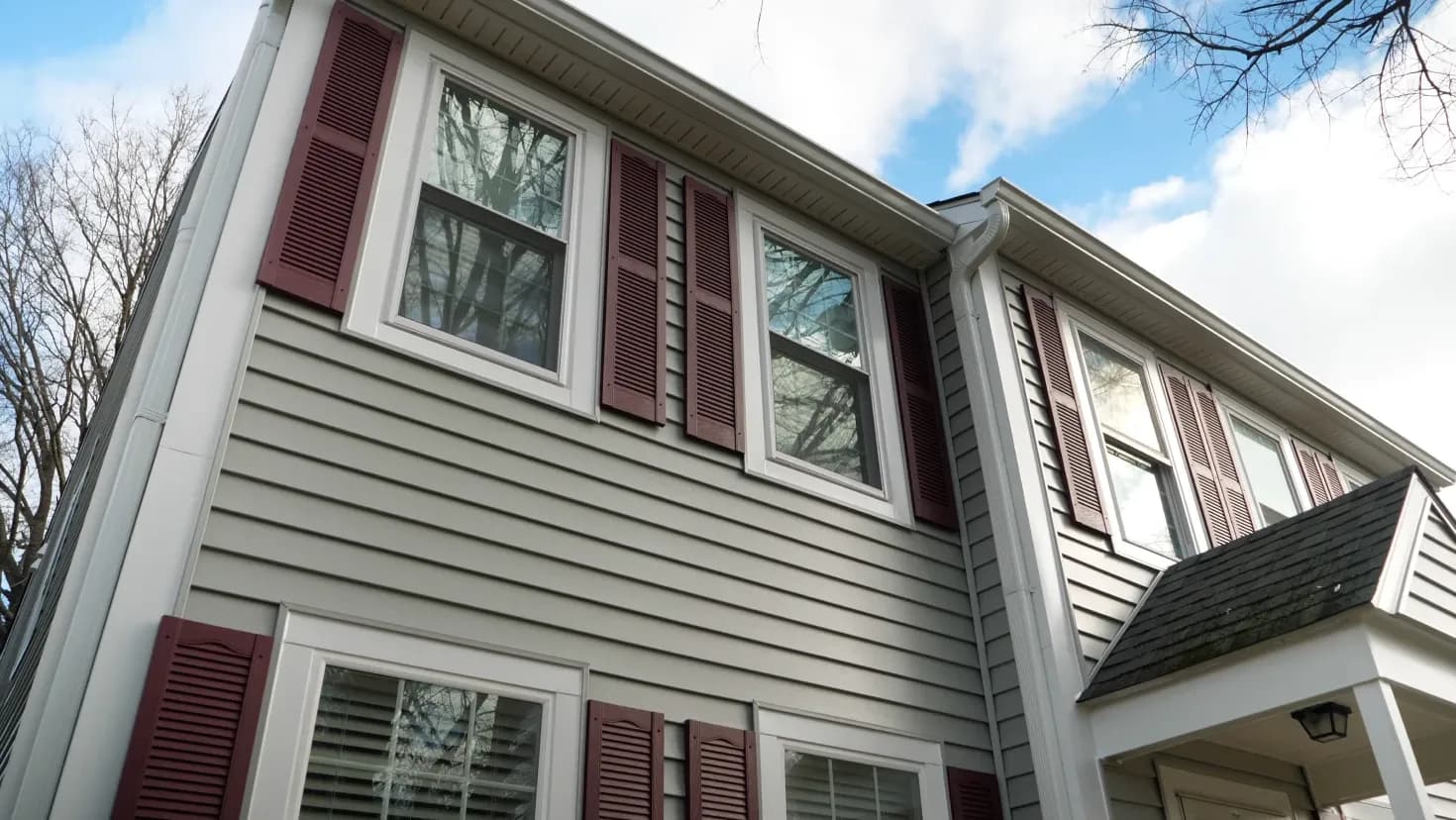 A photo of a light gray colonial-style house with dark red shutters.