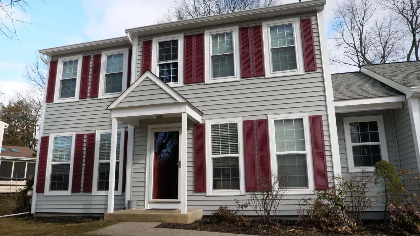 A photo of a light gray colonial-style house with dark red shutters.
