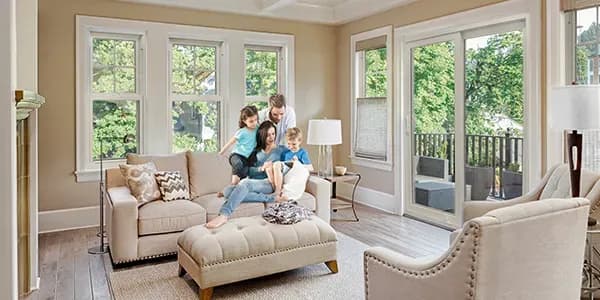 A family in a living room with a couch and large double hung windows.
