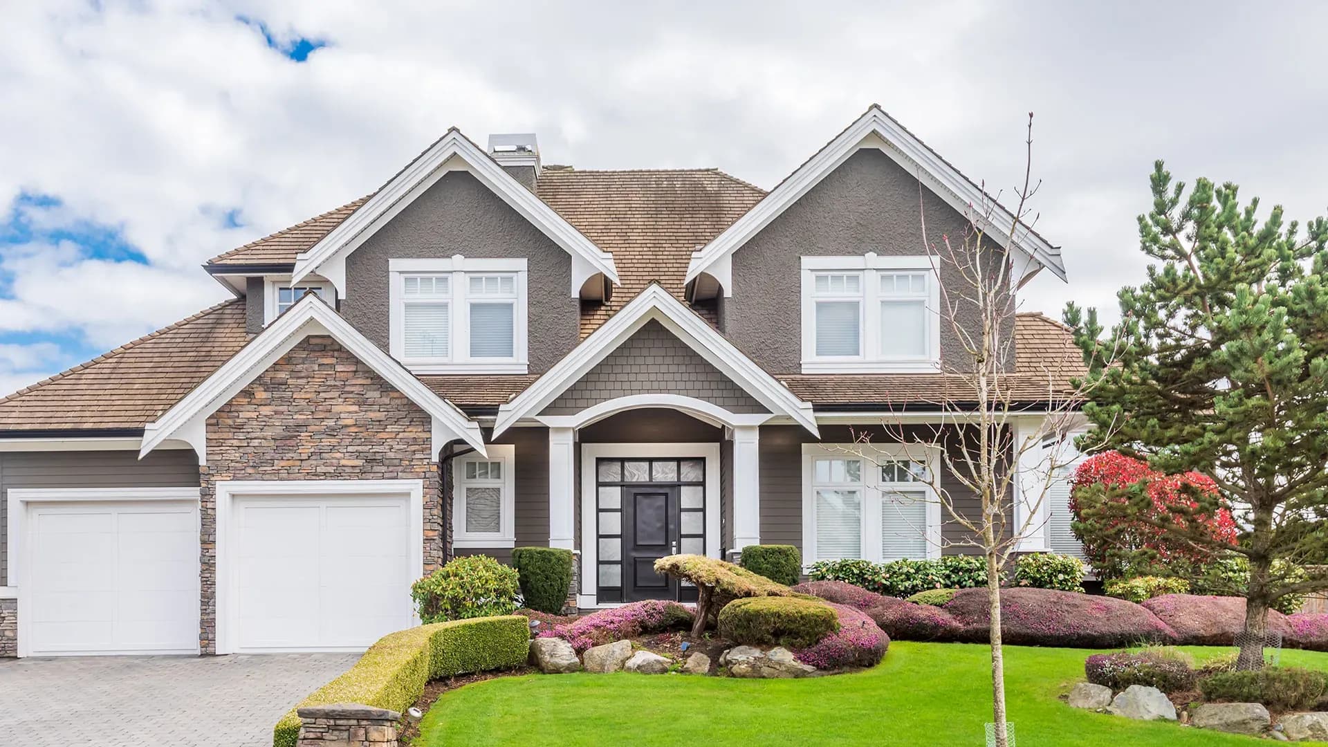 An exterior shot of a brown house with two car garage and stone work.
