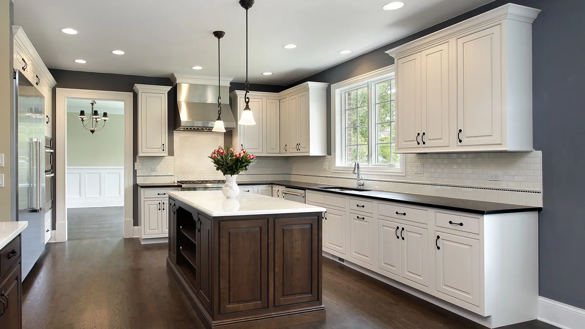A kitchen with white cabinets and trim, a large dark wood island, and dark gray walls.