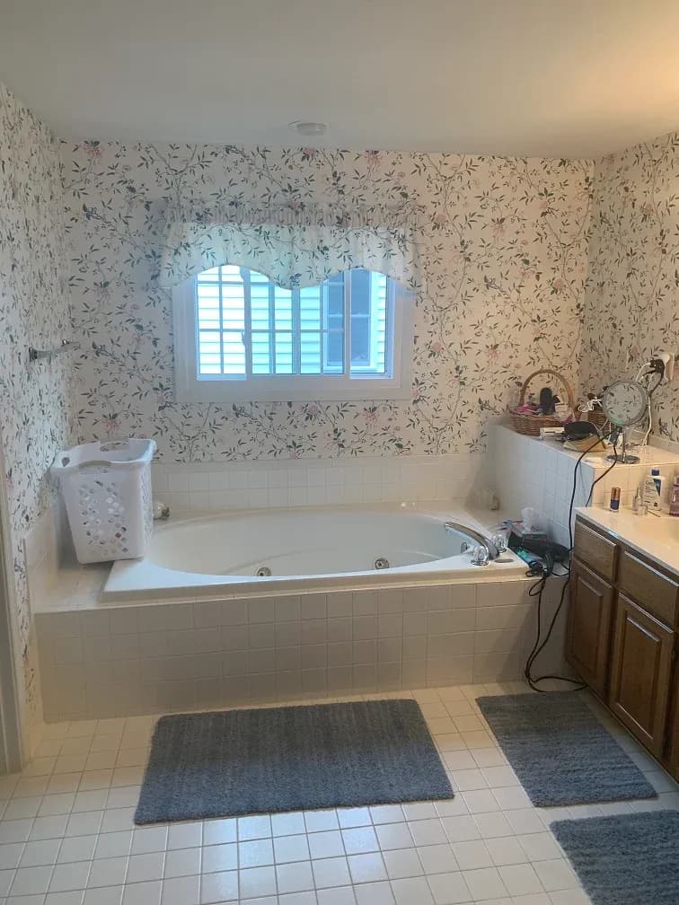 A photo of a jacuzzi-style bathtub with white tiles and floral wallpaper.