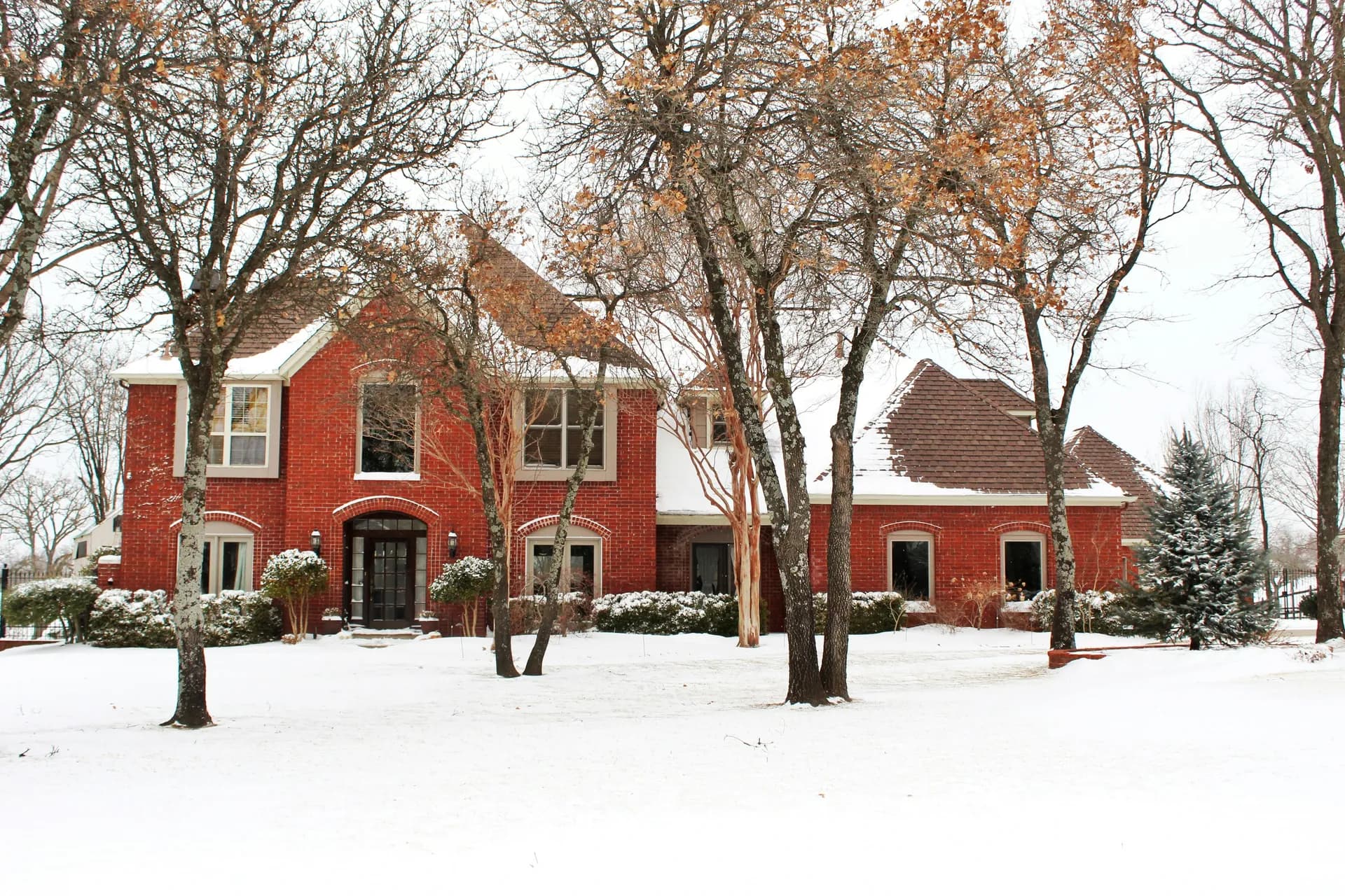 Brick home in the DC metro area during winter with snow-covered yard and bare trees, highlighting potential cold weather damage risks like roof stress, frozen gutters, and exterior wear after the holidays.