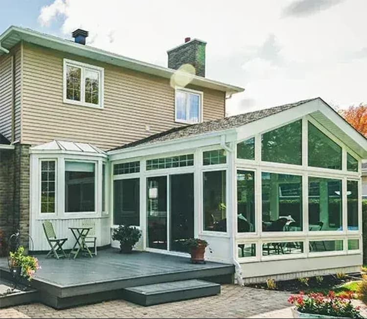 Modern sunroom attached to a house with large windows and white frame, example of a home addition that affects sunroom construction cost