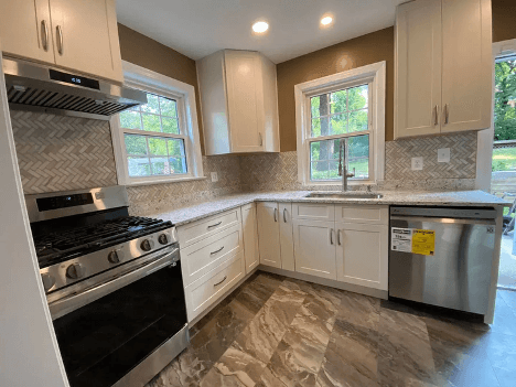 Modern kitchen with cream-colored cabinets, stainless steel appliances, herringbone tile backsplash, and wood-look flooring