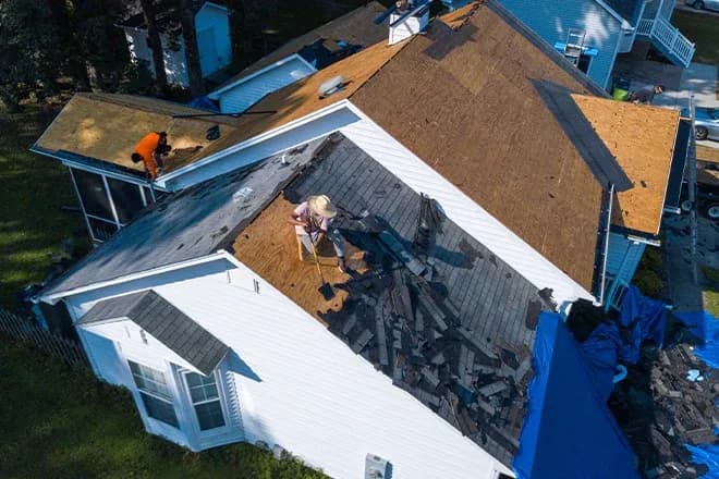 Workers removing roof shingles as part of roof a replacement.