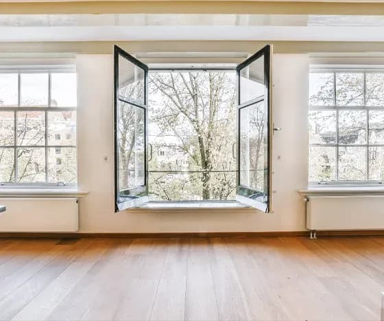 A large open-door window with two large windows on either side looks out on Spring trees in blossom.