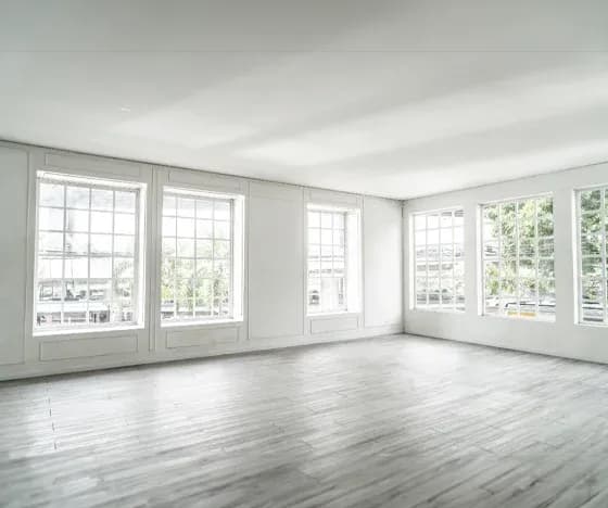 The corner of a spacious, empty room with six large windows letting in lots of light.