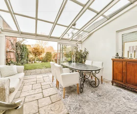 A glass sunroom addition with a dining table and chairs looking out into a yard.