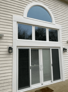 White exterior door with three glass panes and arched transom window above, mounted on horizontal siding with exterior lighting fixtures on either side