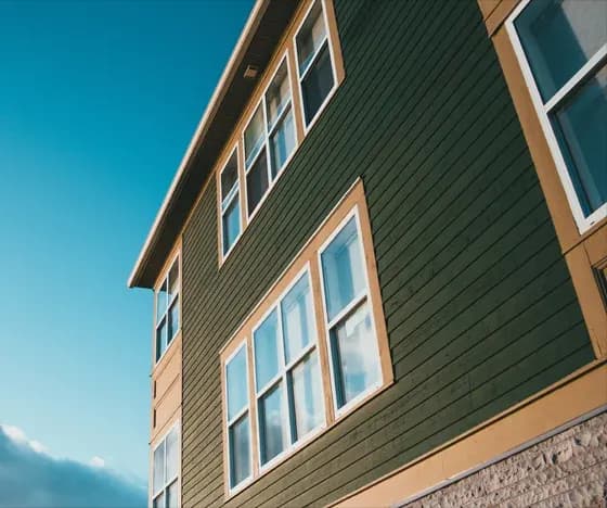 An upward-angled photo of the exterior of a house with Dark brown siding and light brown trim around the windows.