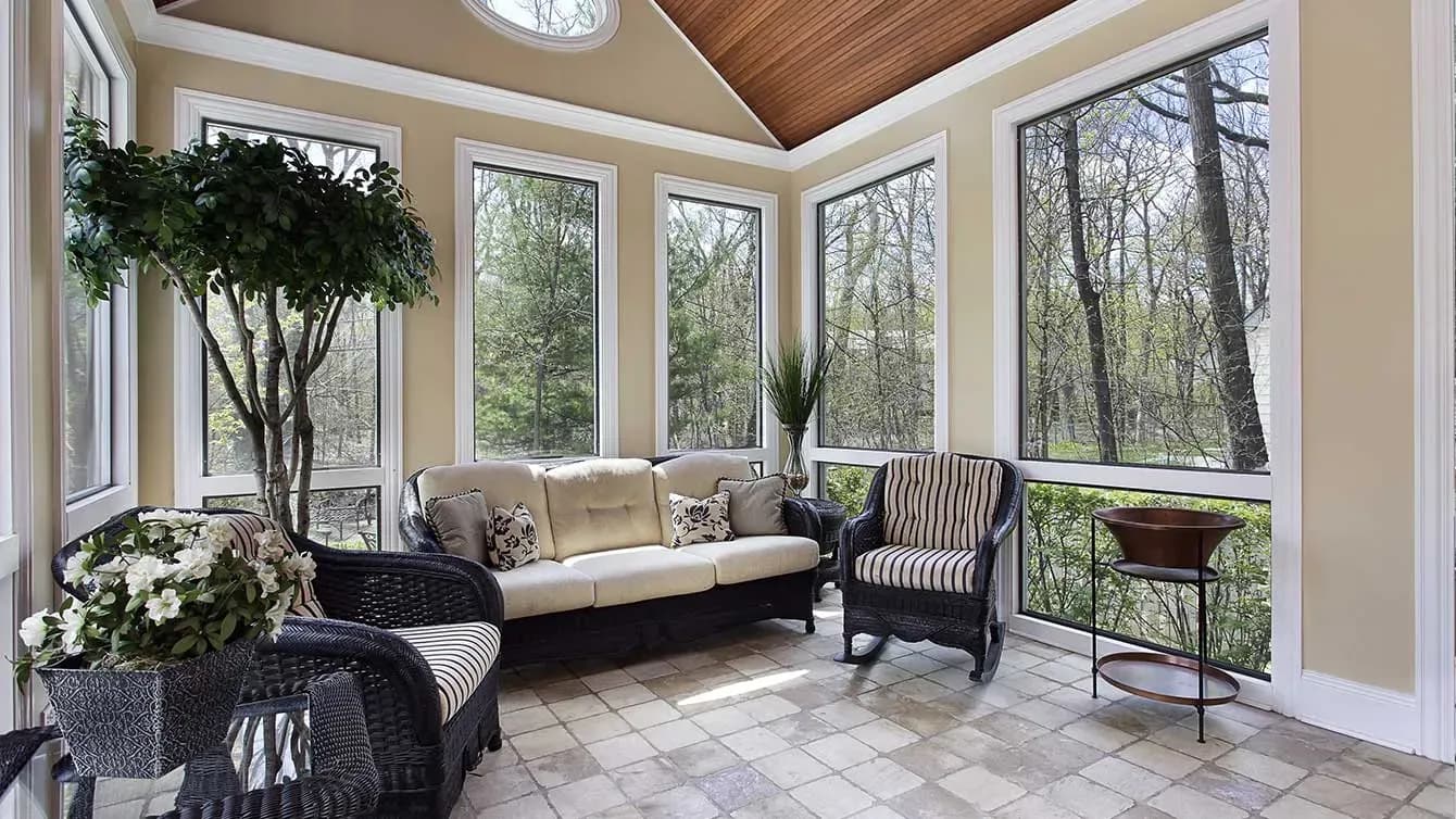 A sunroom with large picture windows, a stone tile floor, and black and white patio furniture.