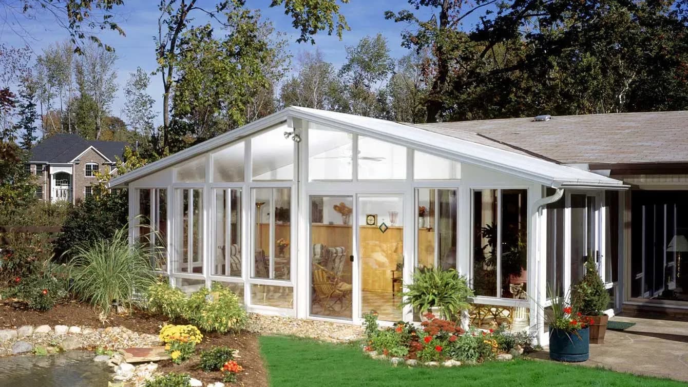 A glass sunroom with patio furniture viewed from the outside.